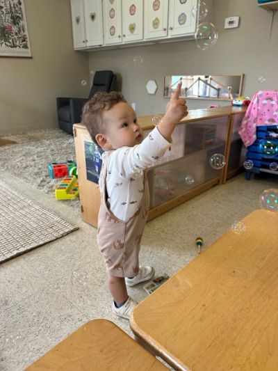 Toddler reaching toward bubbles in the classroom